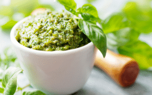 Torn basil leaves on a bowl of pesto