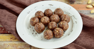Homemade nutty bliss balls made with dates, almonds, and cocoa, in a white plate wooden board.