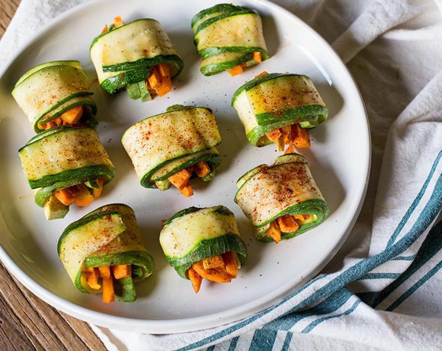 Fresh zucchini rolls filled with carrots and green vegetables, served as a healthy low-carb plant-based snack or appetizer.